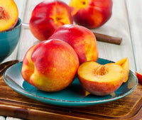 Nectarine 'Nectarina™' with smooth golden-yellow skin and bold red streaks displayed whole and halved on turquoise plate