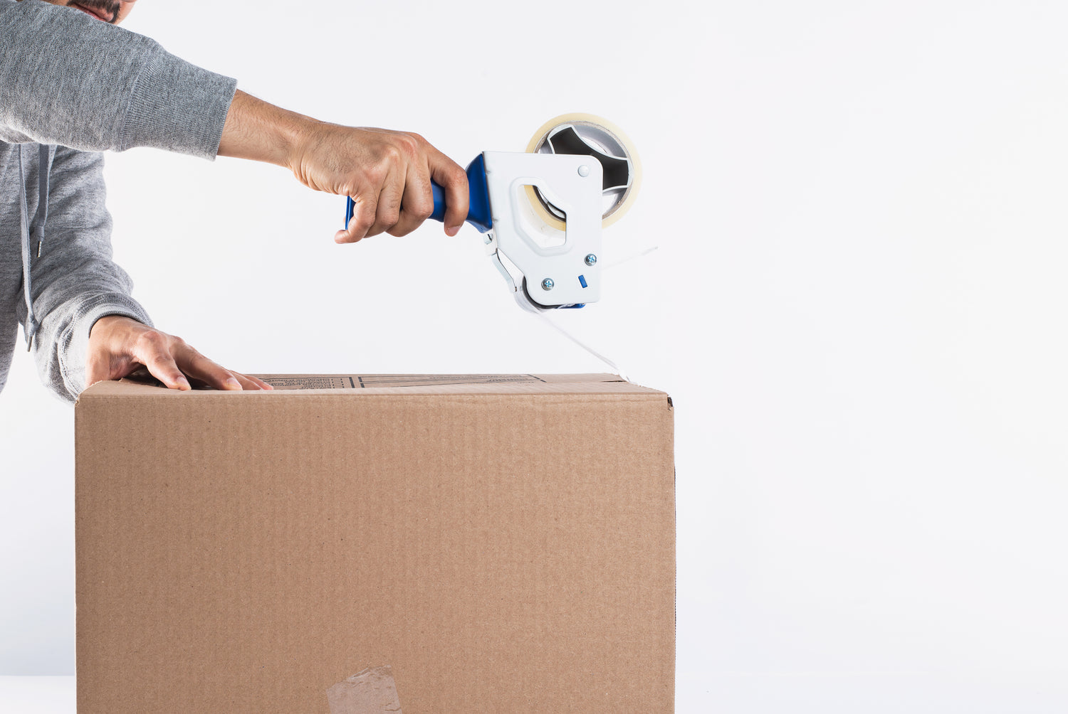 Person sealing a large cardboard box with clear packing tape against a white background